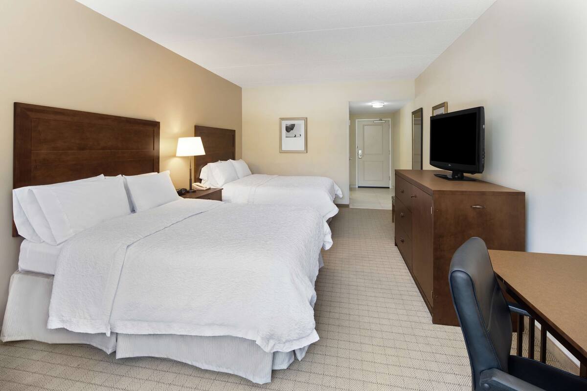 A hotel room with two beds, a desk, a television, and a lamp.
