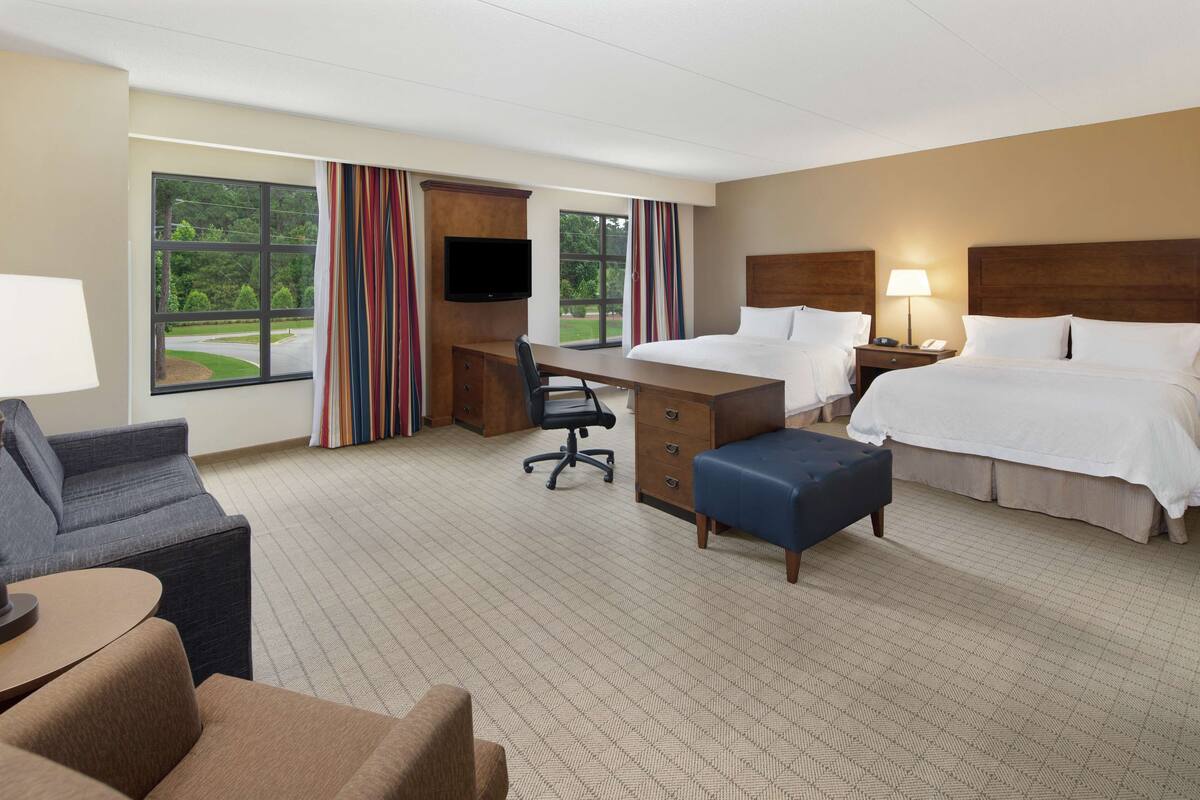 A hotel room with a bed, desk, chair, and a view of the outdoors.