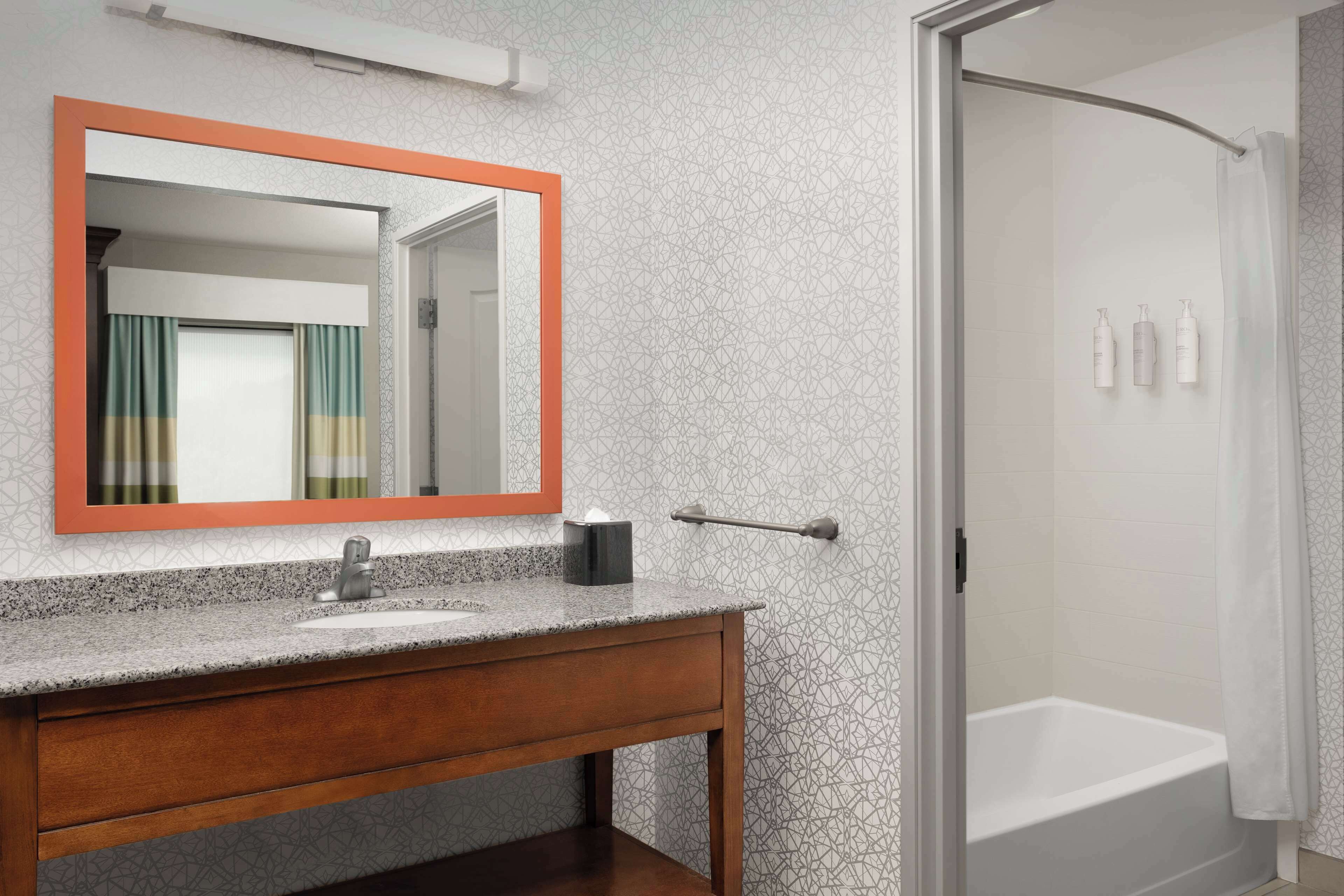 A bathroom with a granite countertop sink, a wooden vanity, a large mirror with an orange frame, and a glass-enclosed shower area.