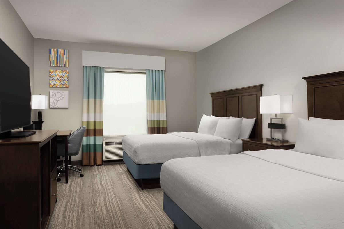 A hotel room with two beds, a desk, a chair, and a TV.
