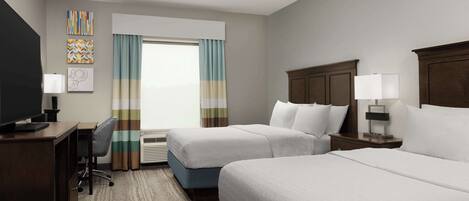 A hotel room with two beds, a desk with a chair, a TV, and artwork on the walls.