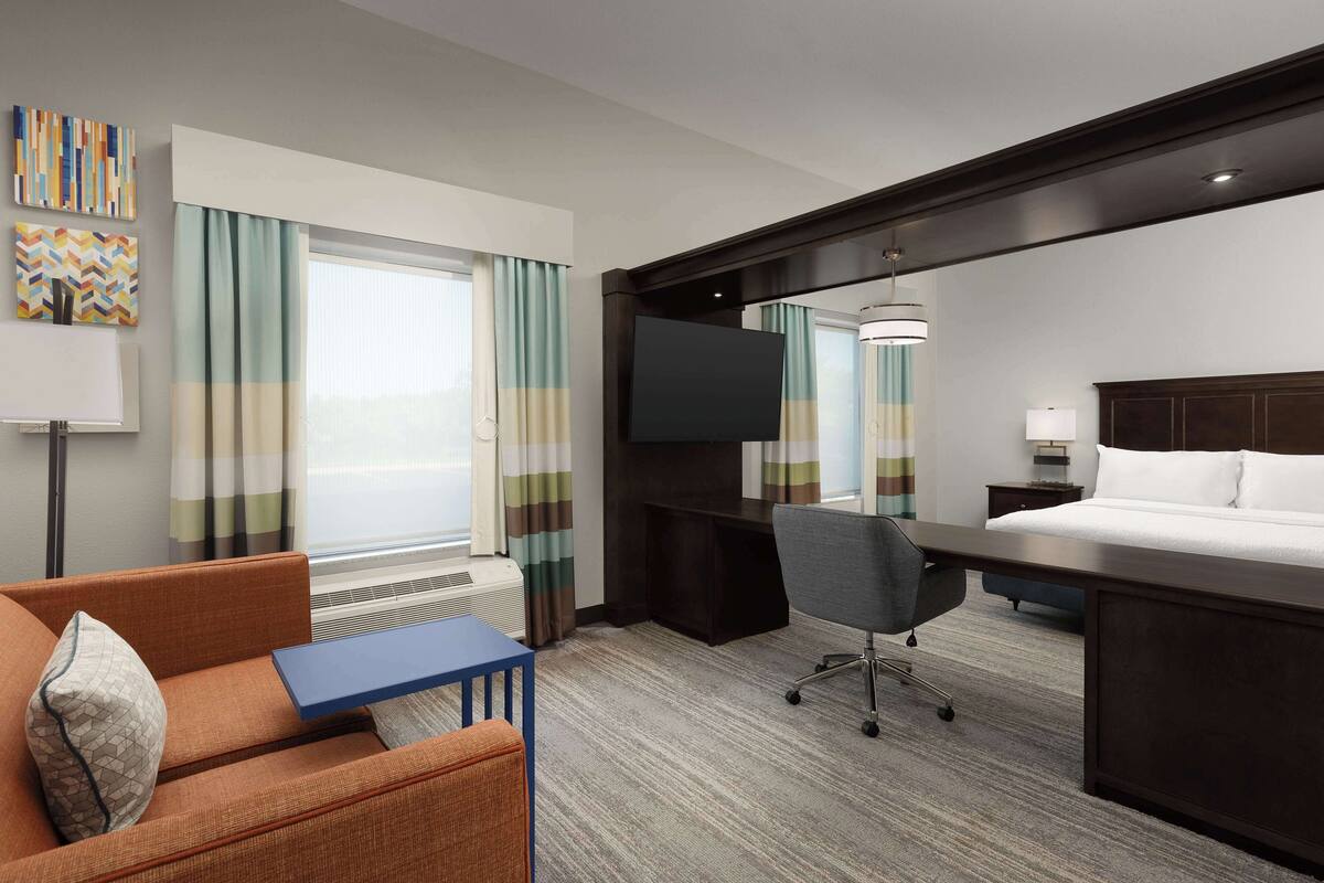 A hotel room with a bed, a desk, a chair, a TV, and a sofa.