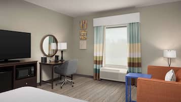 Habitación de hotel con cama, escritorio con silla, televisor, ventana con cortinas y radiador.