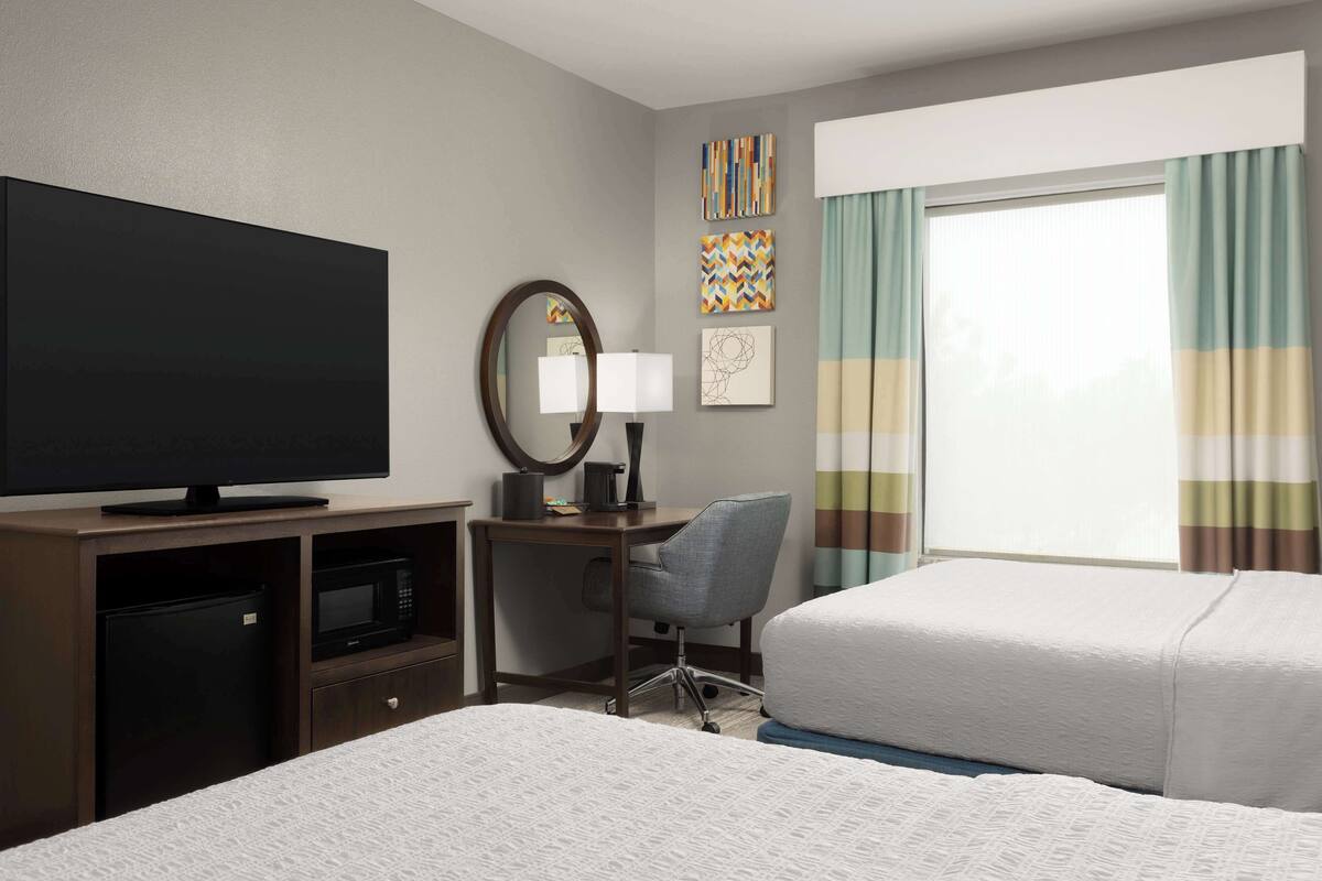 A hotel room with a bed, a desk with a computer, a television, and a window with curtains.