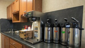 A kitchen with a coffee machine, stainless steel dispensers, wooden cabinets, and a sink. - Red Roof Inn & Suites Dickinson (Dickinson)