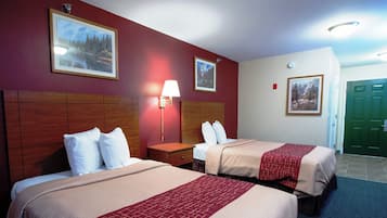 A hotel room with two beds, a nightstand, a lamp, and framed pictures on the walls.