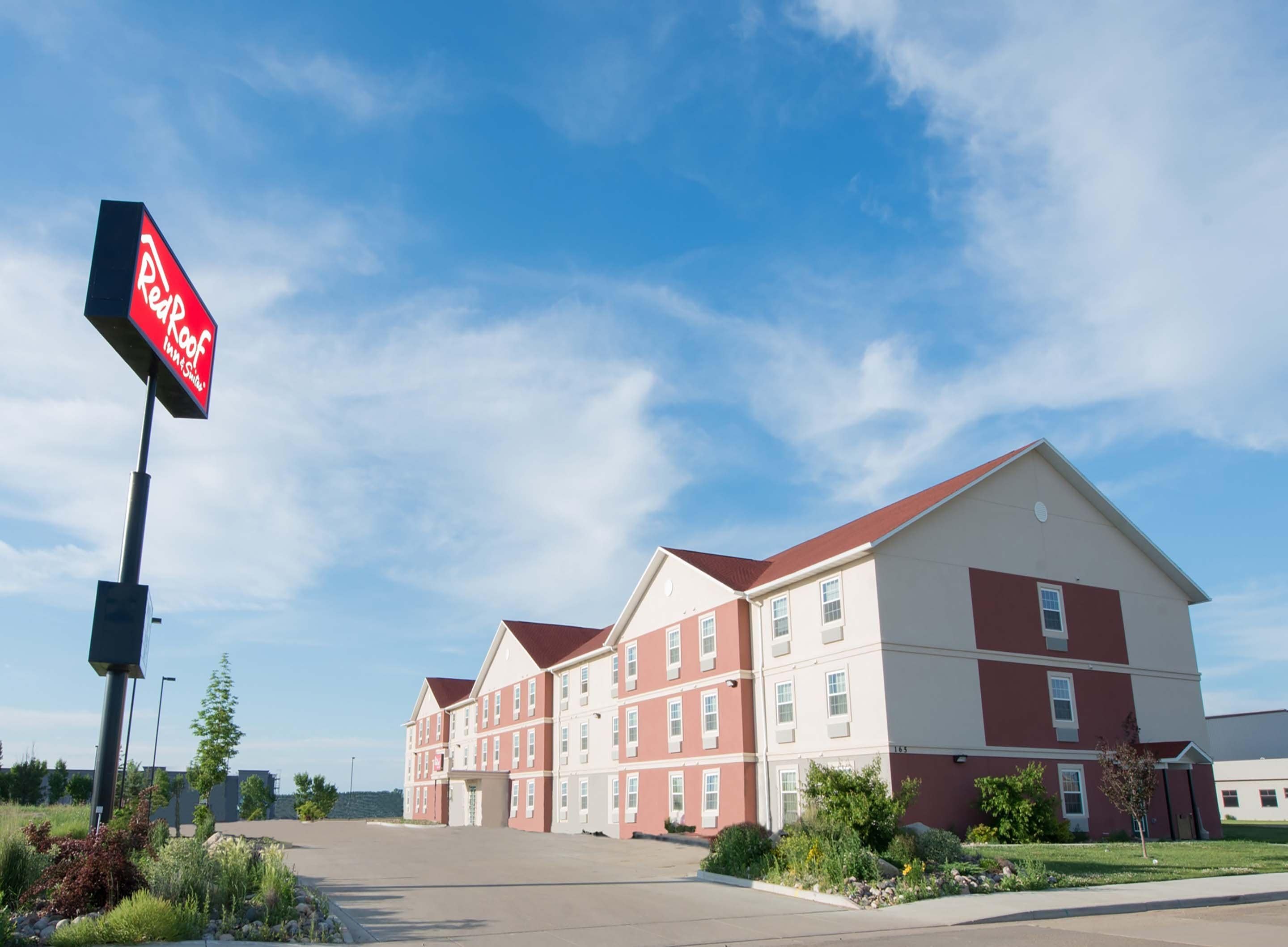 A Red Roof Inn building with a red and white facade, multiple windows, and a clear sky.