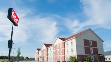A Red Roof Inn building with a red and white facade, multiple windows, and a clear sky.