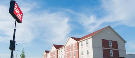 A Red Roof Inn building with a red and white facade, multiple windows, and a clear sky.