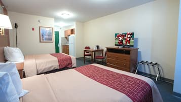 A hotel room with two beds, a desk, a television, and a kitchenette.