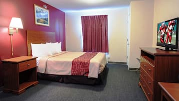 Et hotelværelse med en seng, fjernsyn, skrivebord og lampe.