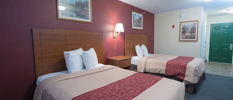 Habitación de hotel con dos camas, una mesita de noche, una lámpara y dos cuadros en la pared.