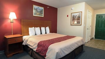 A hotel room with a bed, a nightstand, a lamp, two paintings on the wall, and a green door.