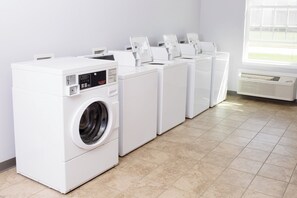 A laundry facility with multiple washing machines and dryers, a tiled floor, and a window providing natural light. - Red Roof Inn & Suites Dickinson (Dickinson)
