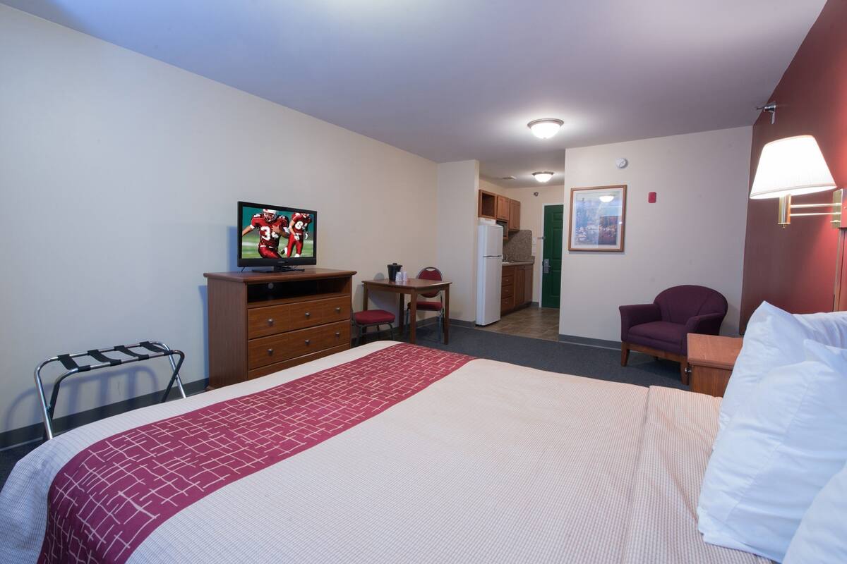 Ein Hotelzimmer mit Bett, Schreibtisch, Stuhl, Fernseher und Küchenzeile.