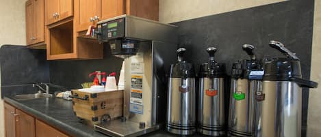 Cozinha equipada com máquina de café, dosadores de aço inoxidável, armários de madeira e pia.