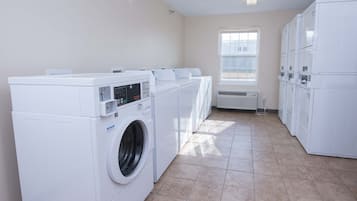 A laundry room with multiple washing machines and dryers, a window, and a tiled floor.