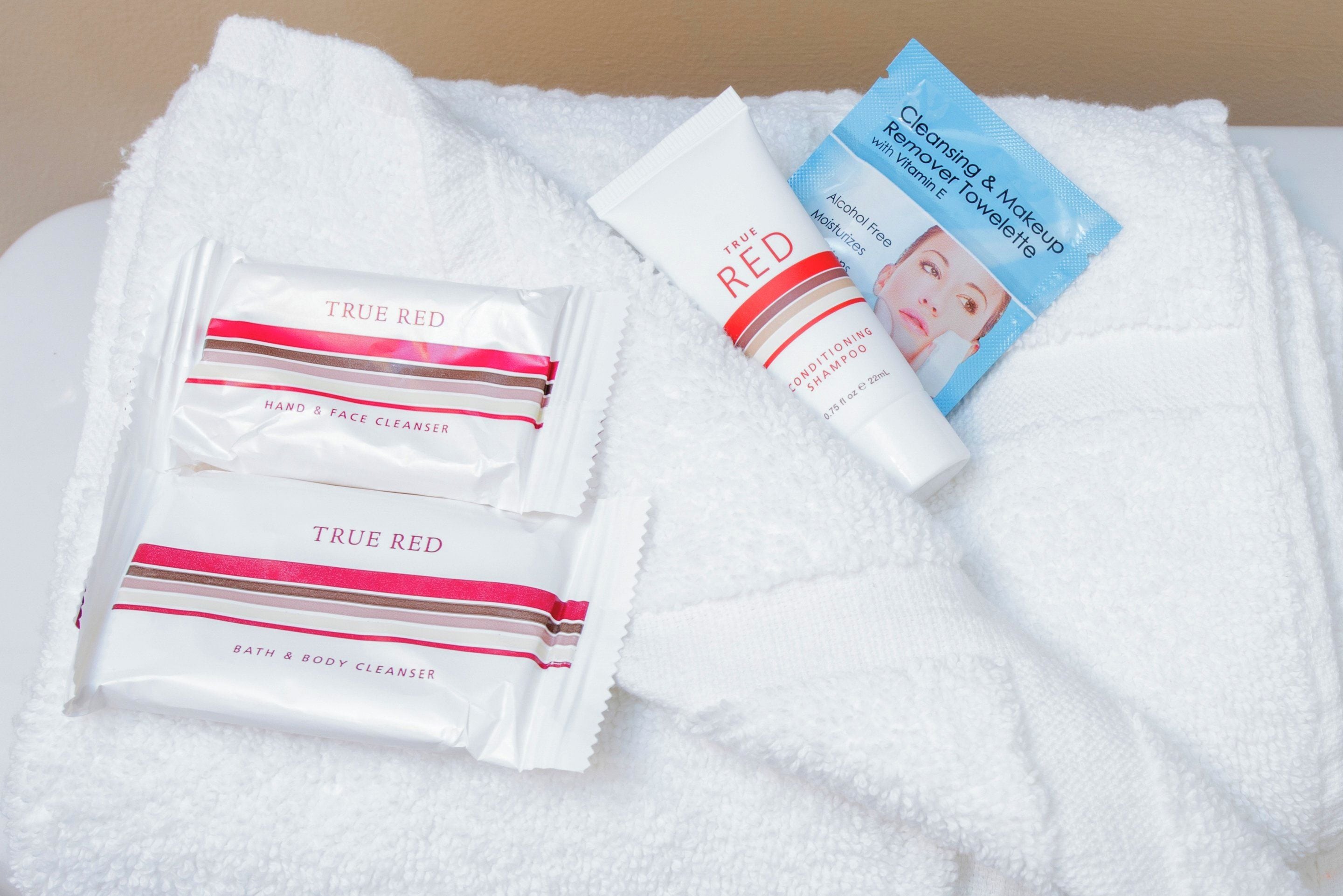 A white towel with toiletries including a hand & face cleanser, a conditioning shampoo, and a cleansing & makeup remover towel.