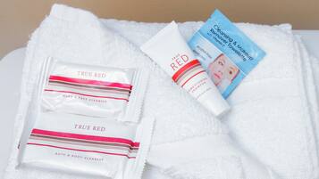 A white towel with toiletries including a hand & face cleanser, a conditioning shampoo, and a cleansing & makeup remover towel.