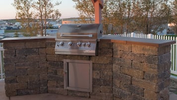 Un barbecue extérieur, avec un mur en pierre et une porte en métal, se dressant sur un fond de verdure et offrant une vue lointaine sur des bâtiments.