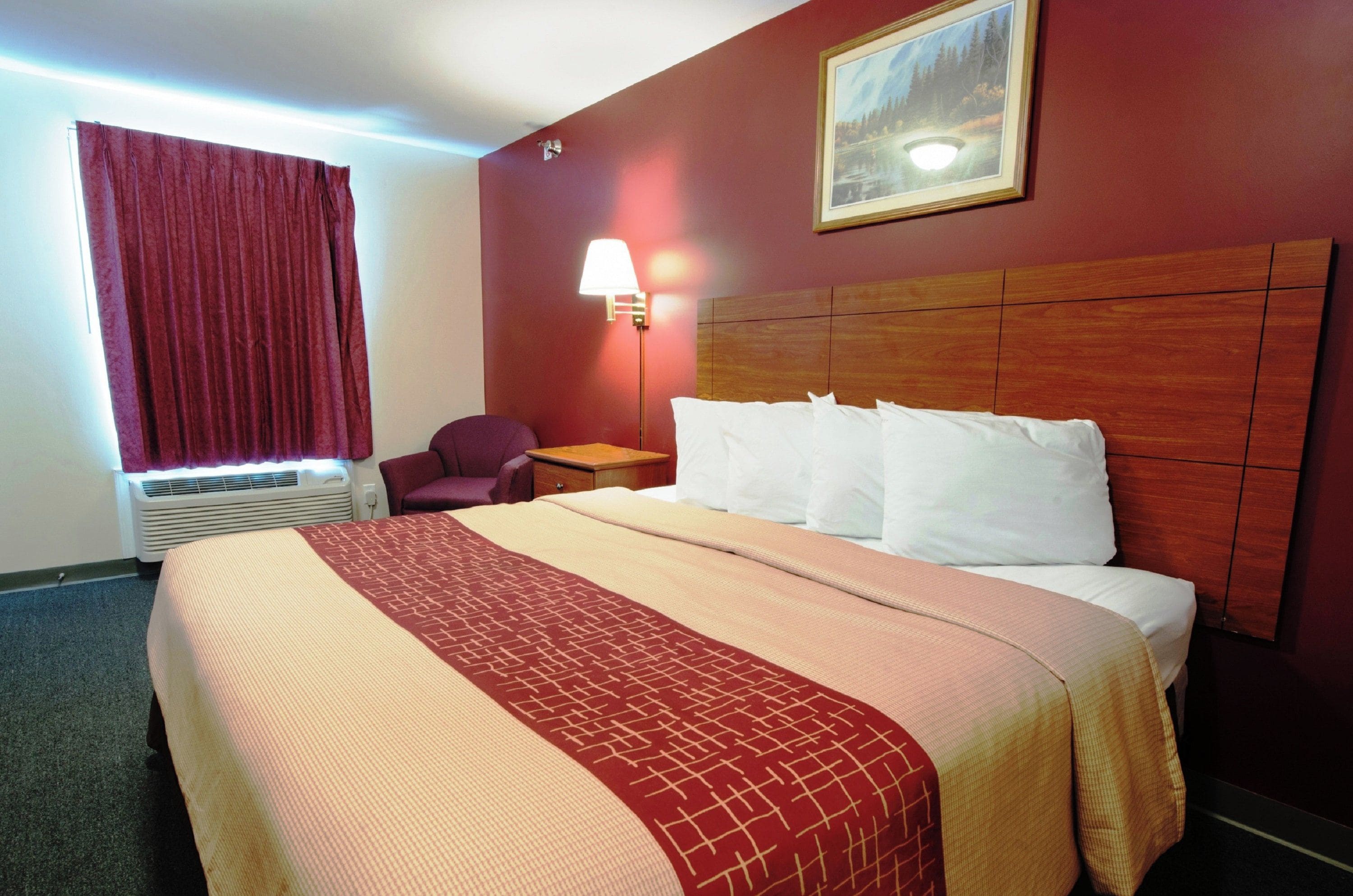 Quarto de hotel com uma cama grande, mesa de cabeceira, abajur, cadeira e janela com cortinas.