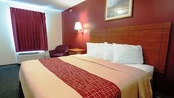 Quarto de hotel com uma cama grande, mesa de cabeceira, abajur, cadeira e janela com cortinas.