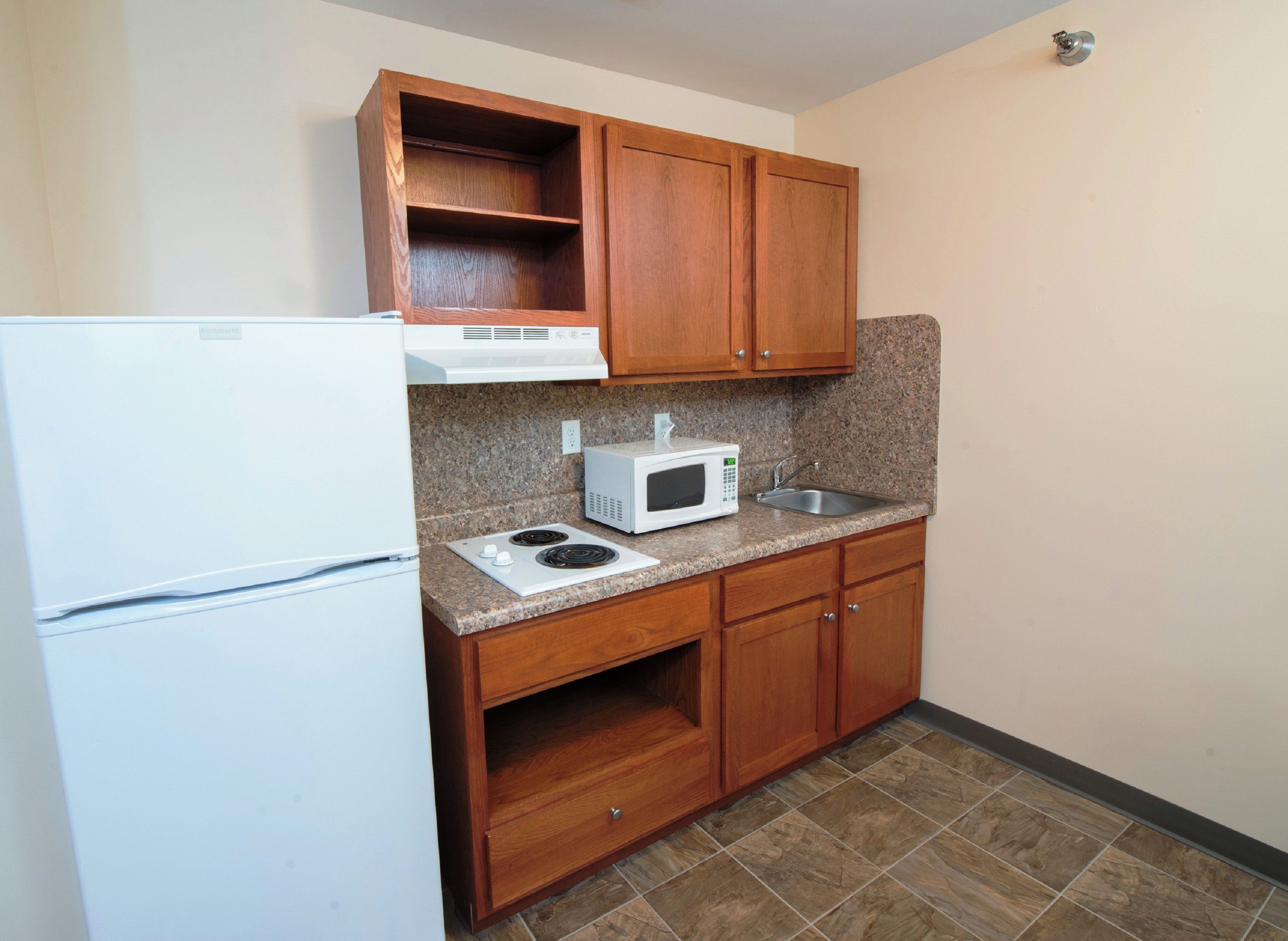 Cocina compacta con microondas integrado, estufa y armarios de madera.