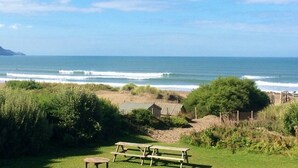 A beach view with picnic tables and a small building in the foreground.