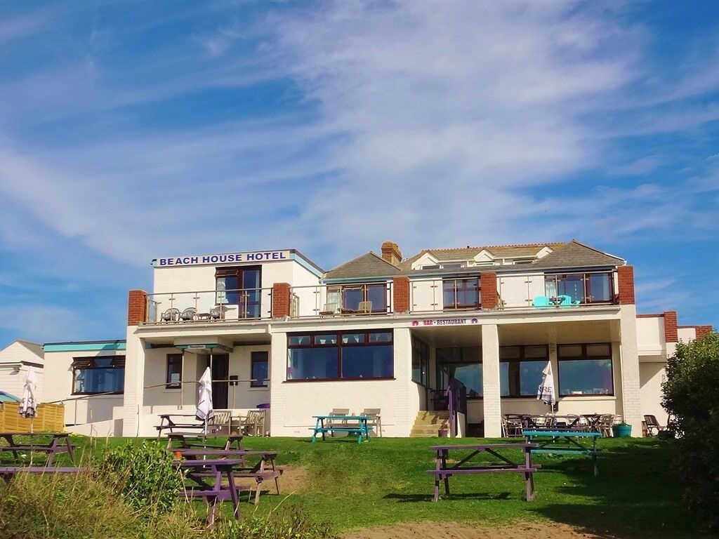 A two-story building with a sign reading "Beach House Hotel" and a restaurant sign below. There are picnic tables in the foreground.