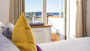 A bedroom with a view of the beach, a bedside table with a bottle and glasses, and a sign above the window that reads "The beach is where my heart is."