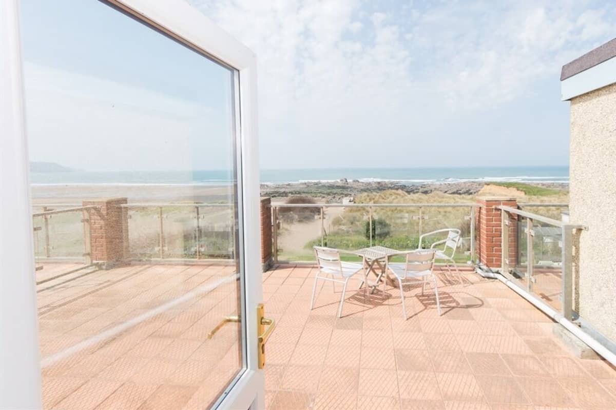 A balcony with a glass door, outdoor seating, and a view of the sea.