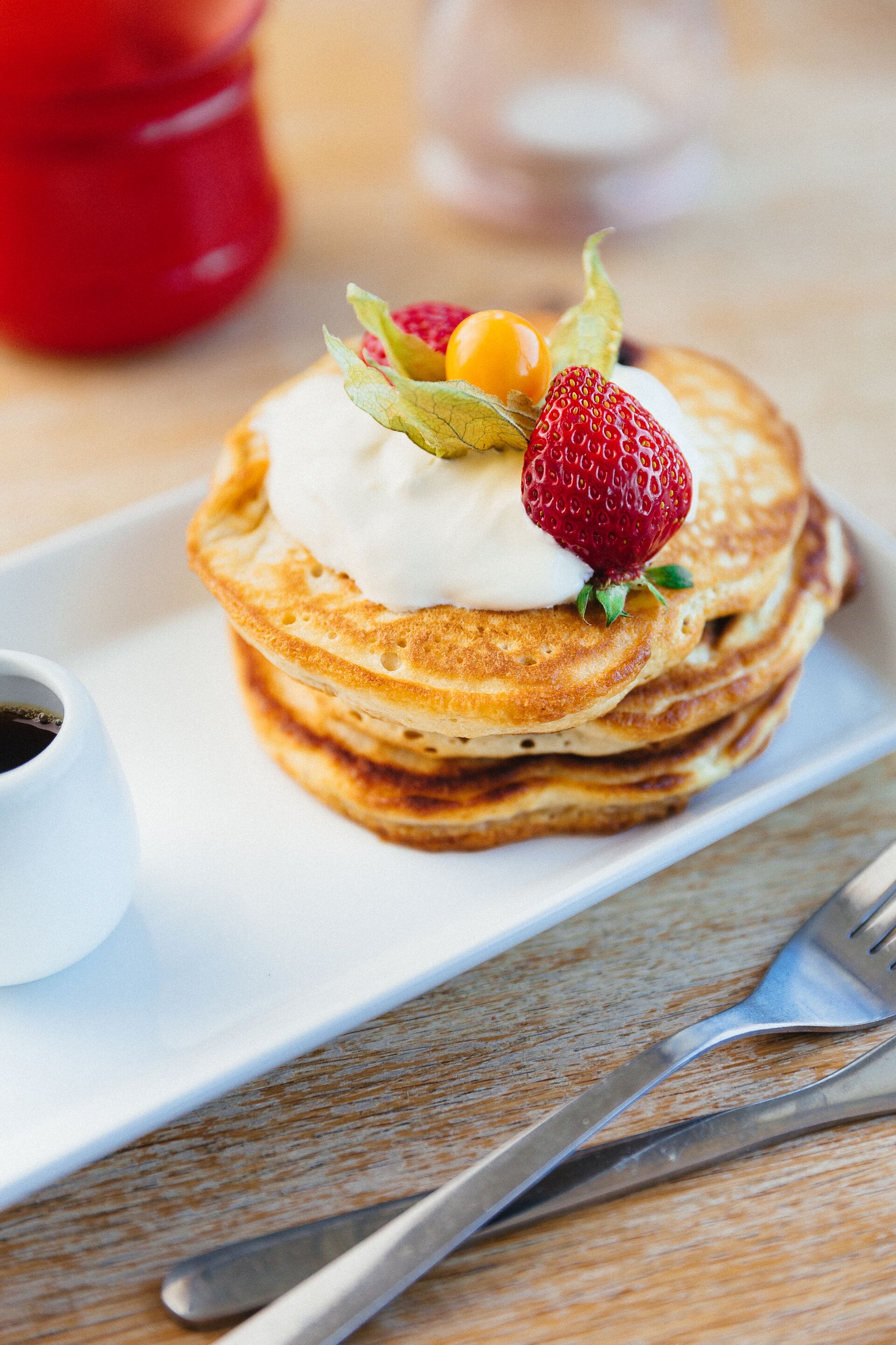 A stack of pancakes with whipped cream and fruit on a white plate.