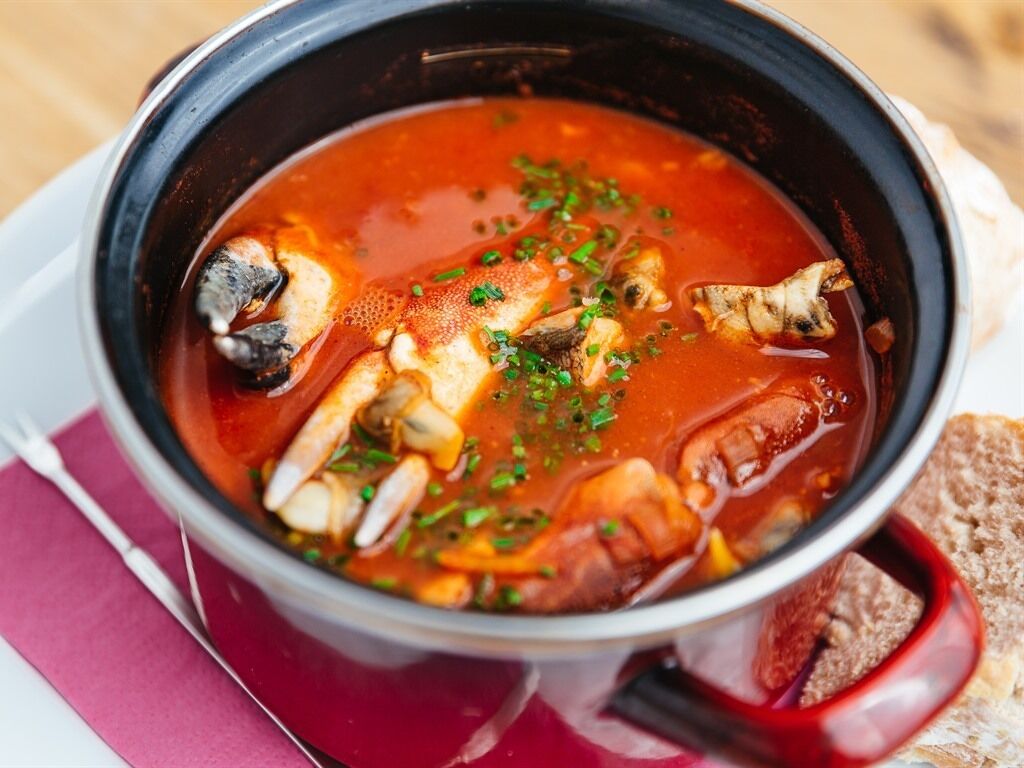 Un bol de soupe aux poissons et aux herbes, accompagné d’une tranche de pain.