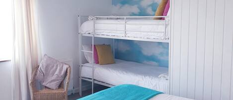 A bunk bed room with a white ceiling, a wall mural of clouds, a wicker chair, and a large bed with a teal blanket.