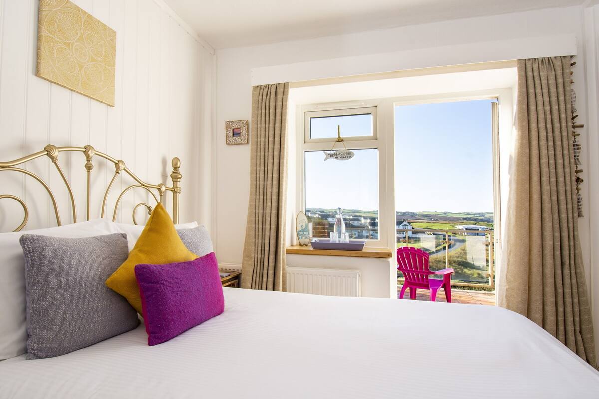 A bedroom with a bed, pillows, a window with a view, and a chair.