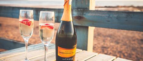 A bottle of wine and two glasses on a wooden table with a beach in the background.