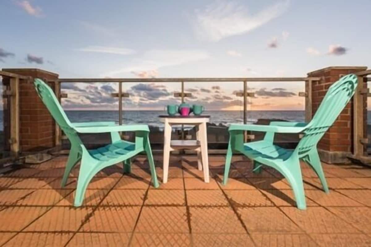 A balcony with two turquoise chairs and a small table with a vase and a bowl.