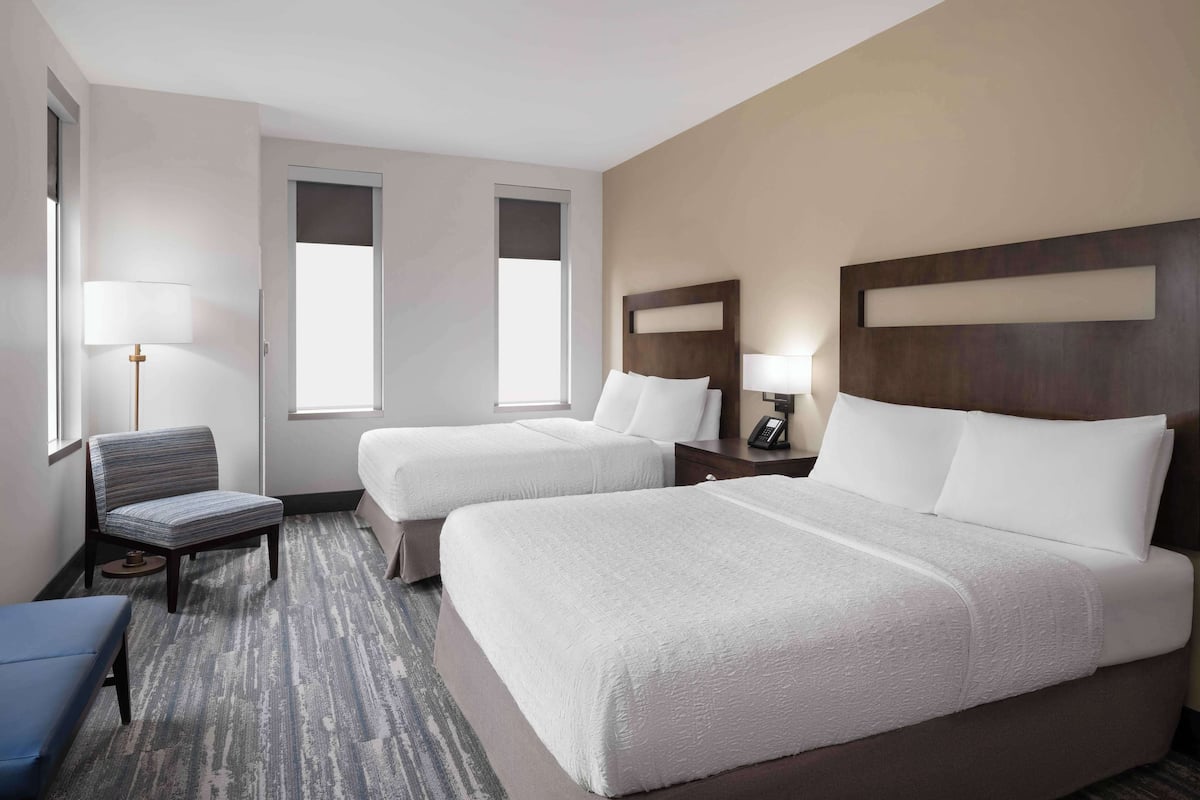 A hotel room with two beds, a chair, a desk, and a lamp.