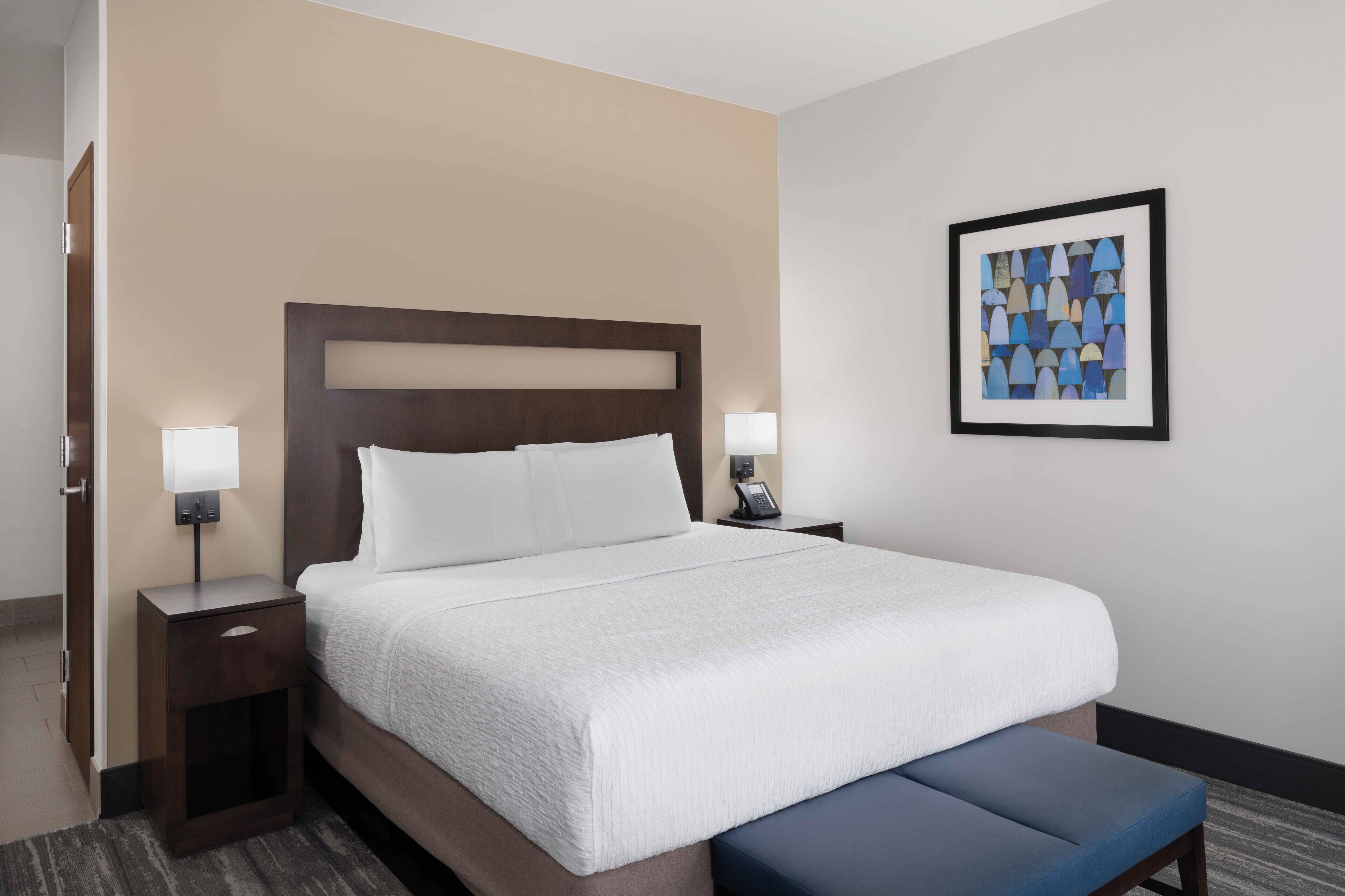 A hotel room with a large bed, two bedside tables, a wall-mounted phone, and a framed artwork.