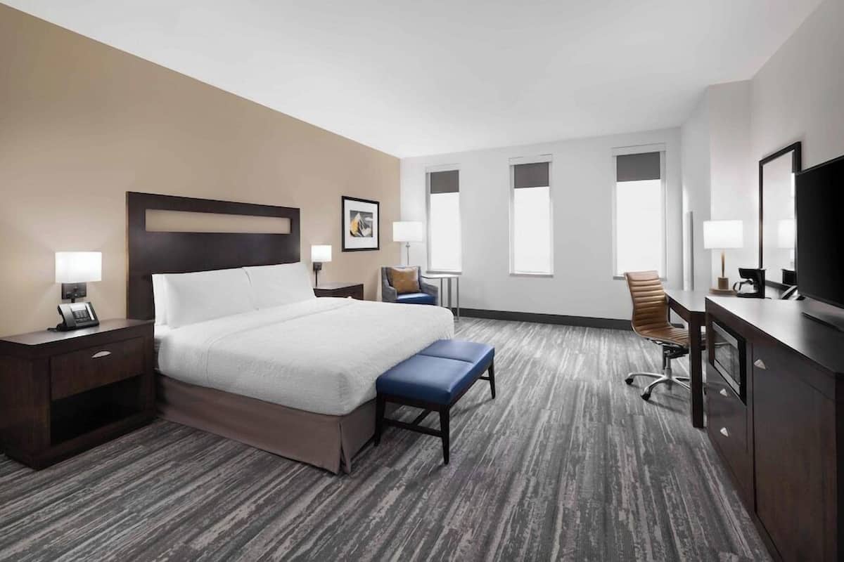 A hotel room with a large bed, a desk, a chair, and a television.