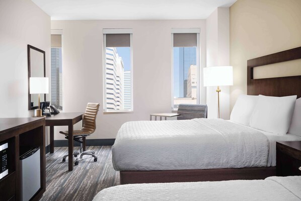 A hotel room with a bed, a desk, a chair, and a window with a view of buildings.