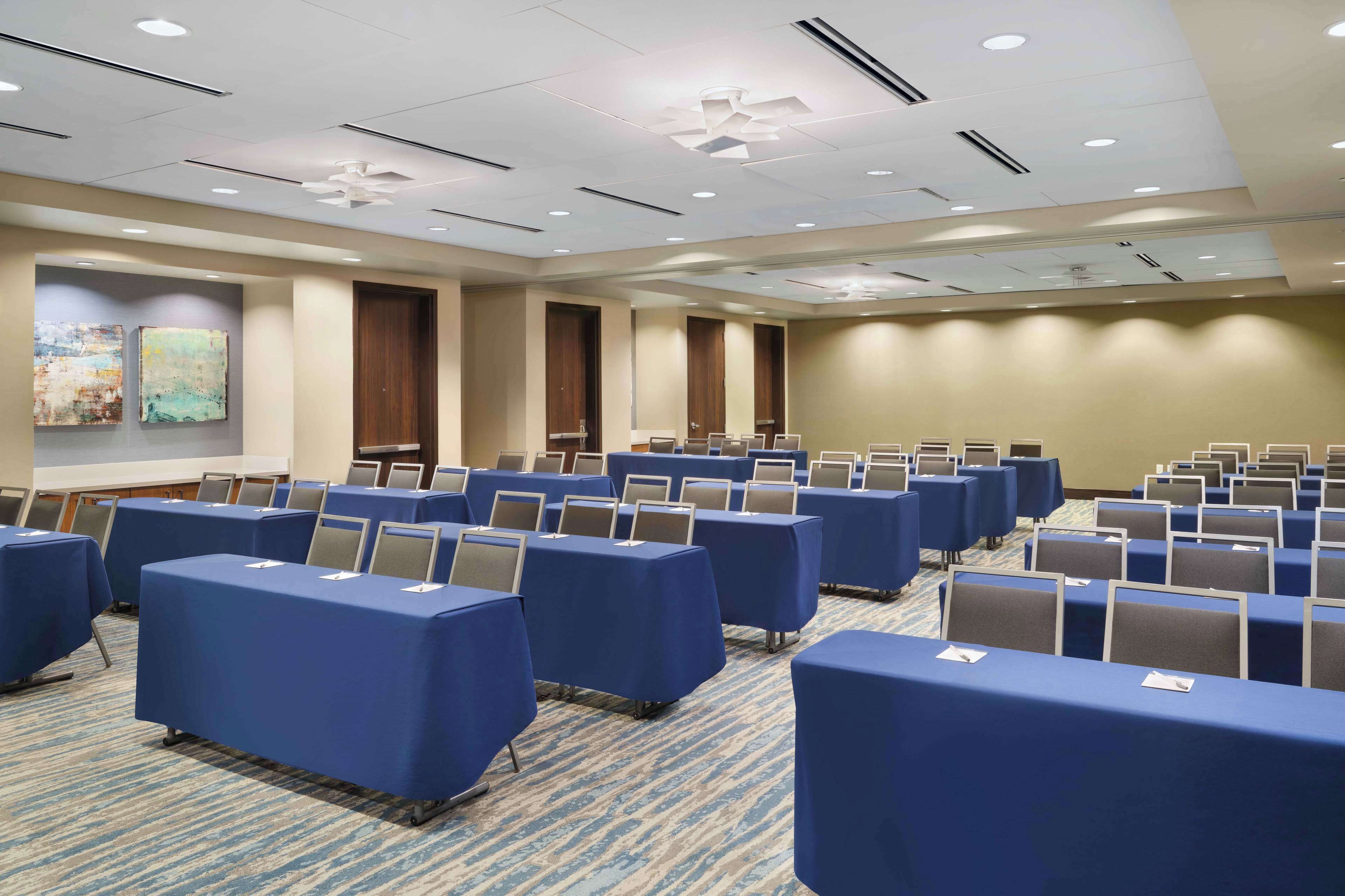 A conference room with rows of tables and chairs, a ceiling fan, and artwork on the walls.