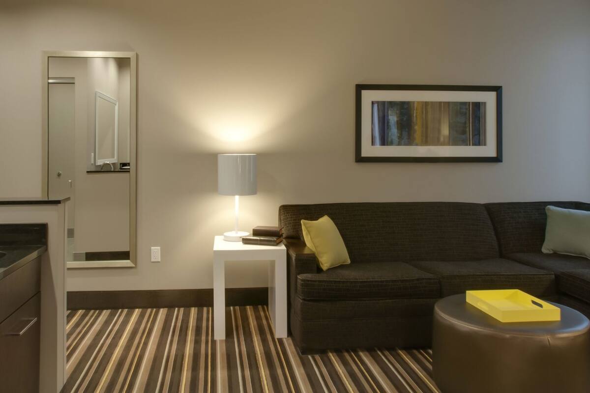 Ein Hotelzimmer mit einer Couch, einem kleinen Tisch mit einer Lampe, einem Spiegel, einem gerahmten Bild und einem Streifenmuster-Teppich.