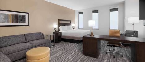 A hotel room with a bed, a sofa, a desk, and a chair.