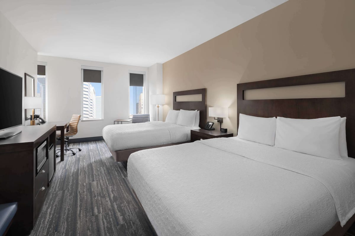 A hotel room with two beds, a desk, a chair, and a TV.
