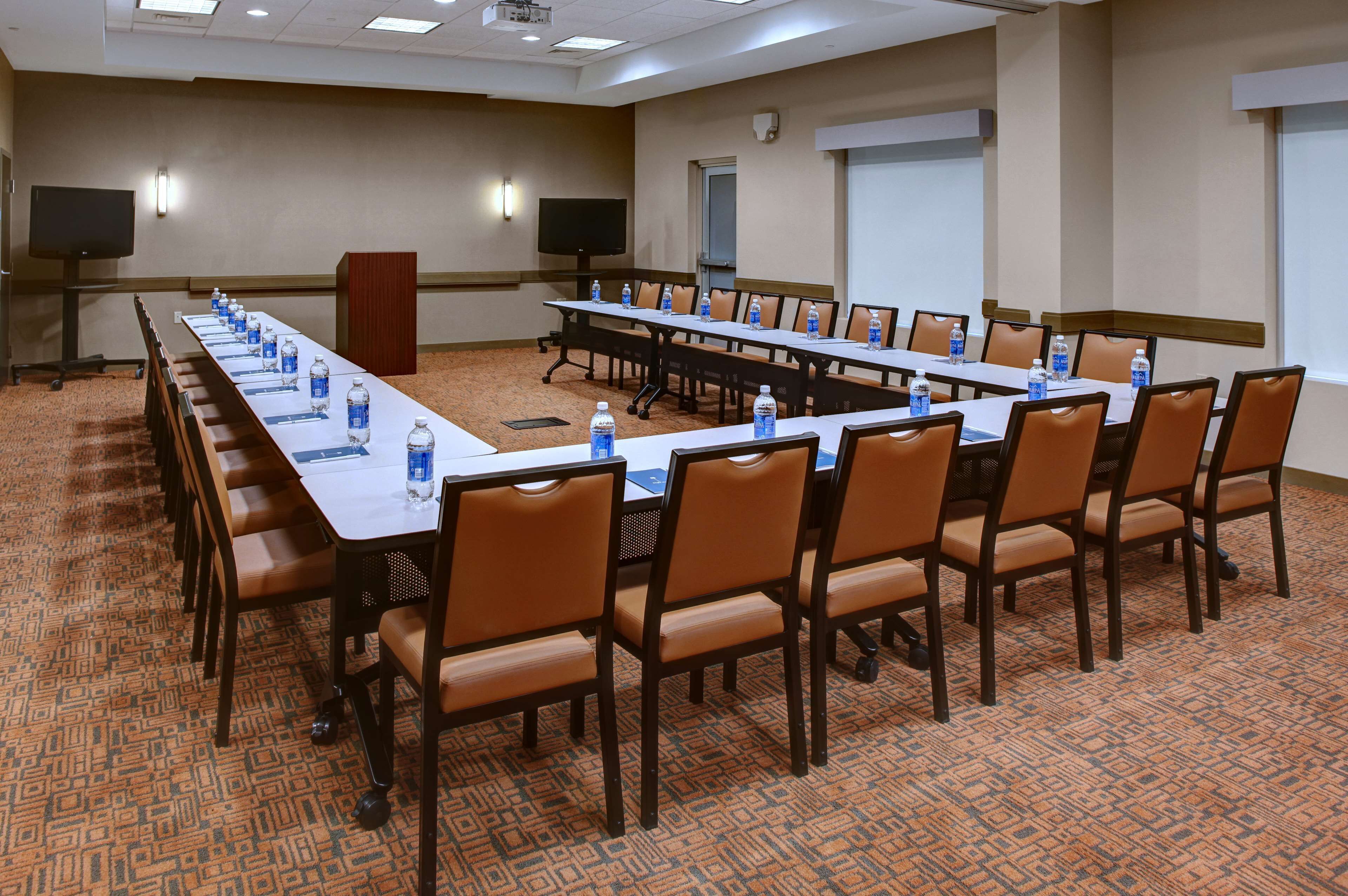 A conference room with a long table, chairs, water bottles, and a projector screen.