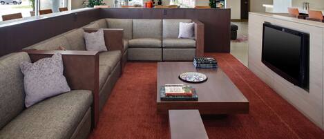 A modern living room with a sectional sofa, a flat-screen TV, and a coffee table with books.
