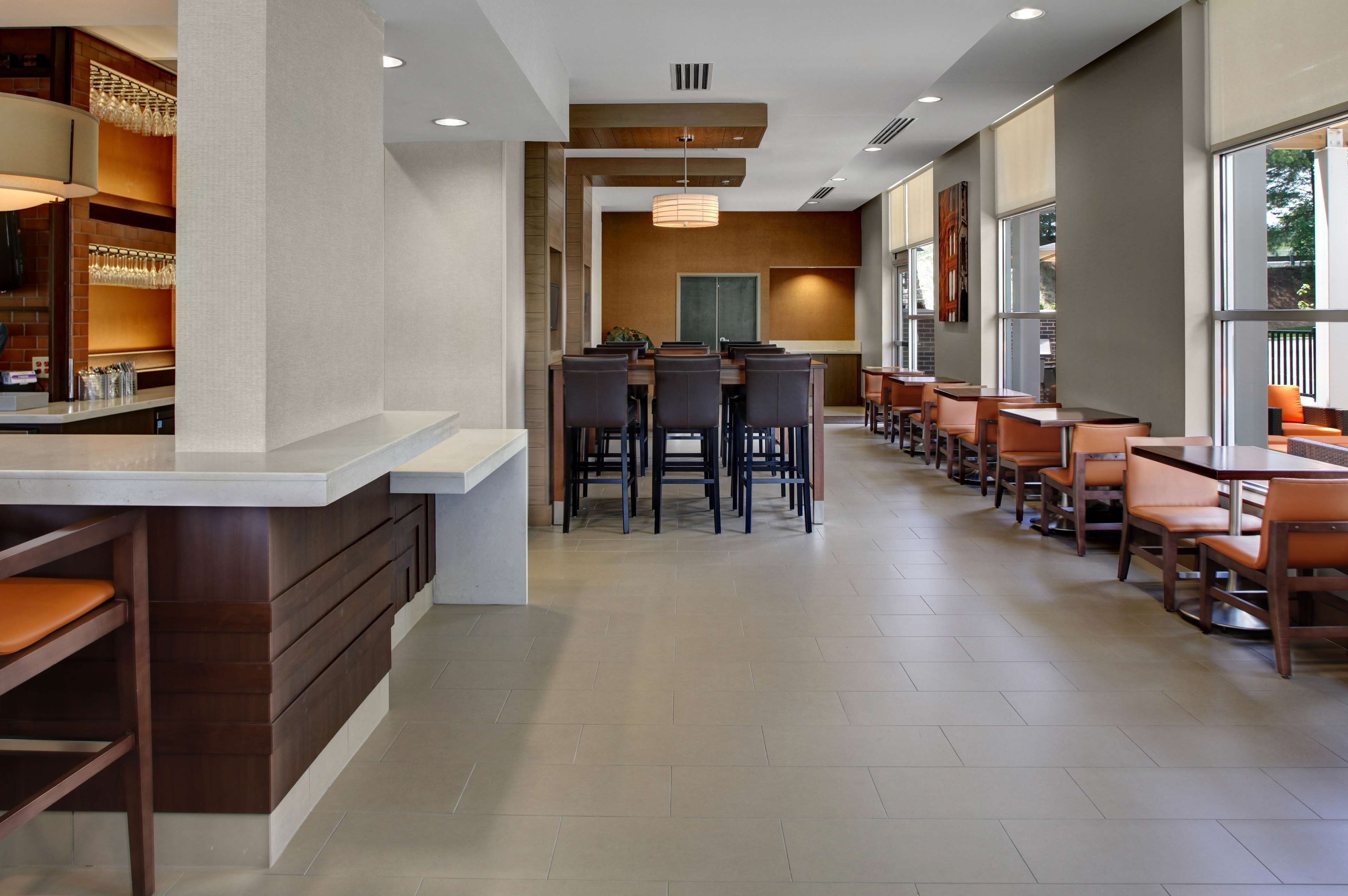 A modern restaurant with a long counter, multiple tables, and chairs.