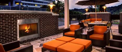 An outdoor patio with a brick fireplace, wicker furniture, and an umbrella.