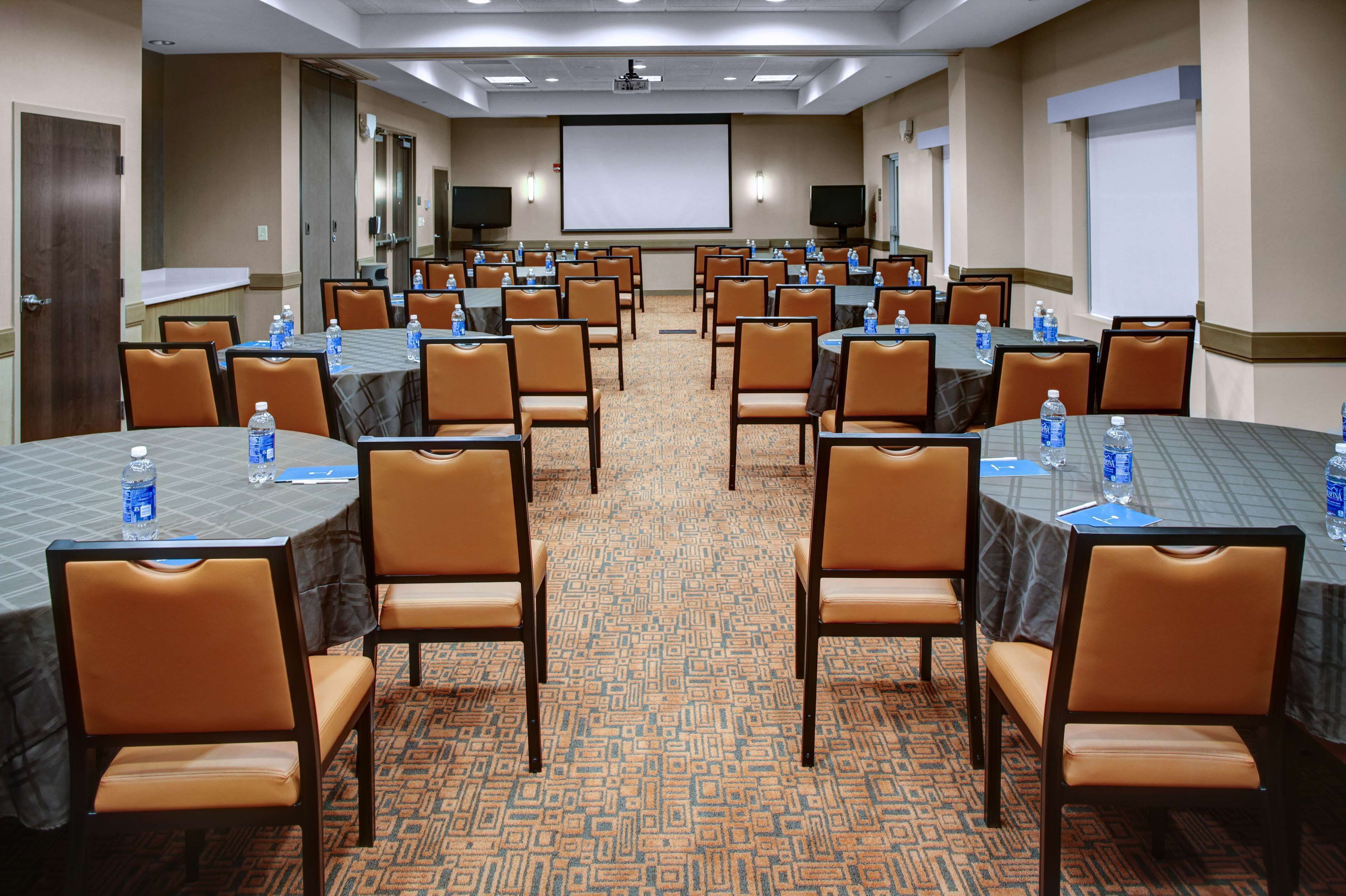 A conference room with multiple tables and chairs, equipped with water bottles and projectors.